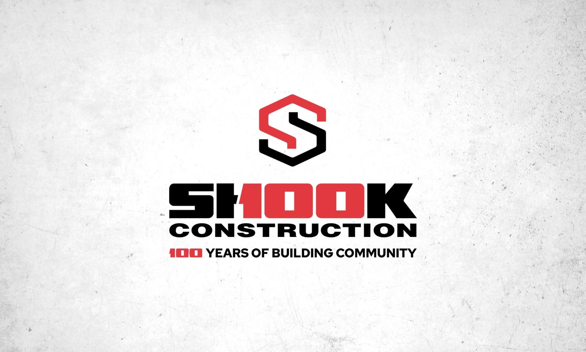 Shook Construction logo with a red and black S symbol above the name. Text reads Shook Construction 100 Years of Building Community with 100 highlighted in red. White textured background.