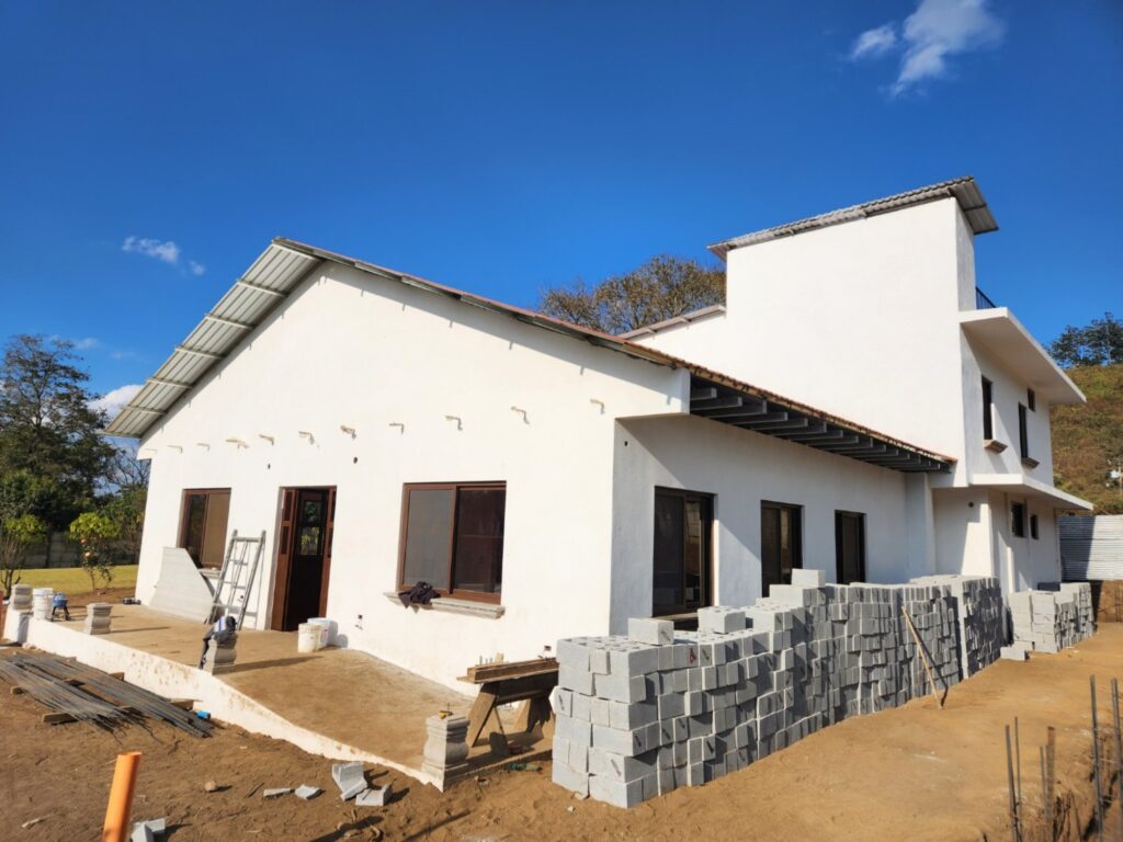 A white house under construction with stacked concrete blocks and building materials outside, set against a clear blue sky.