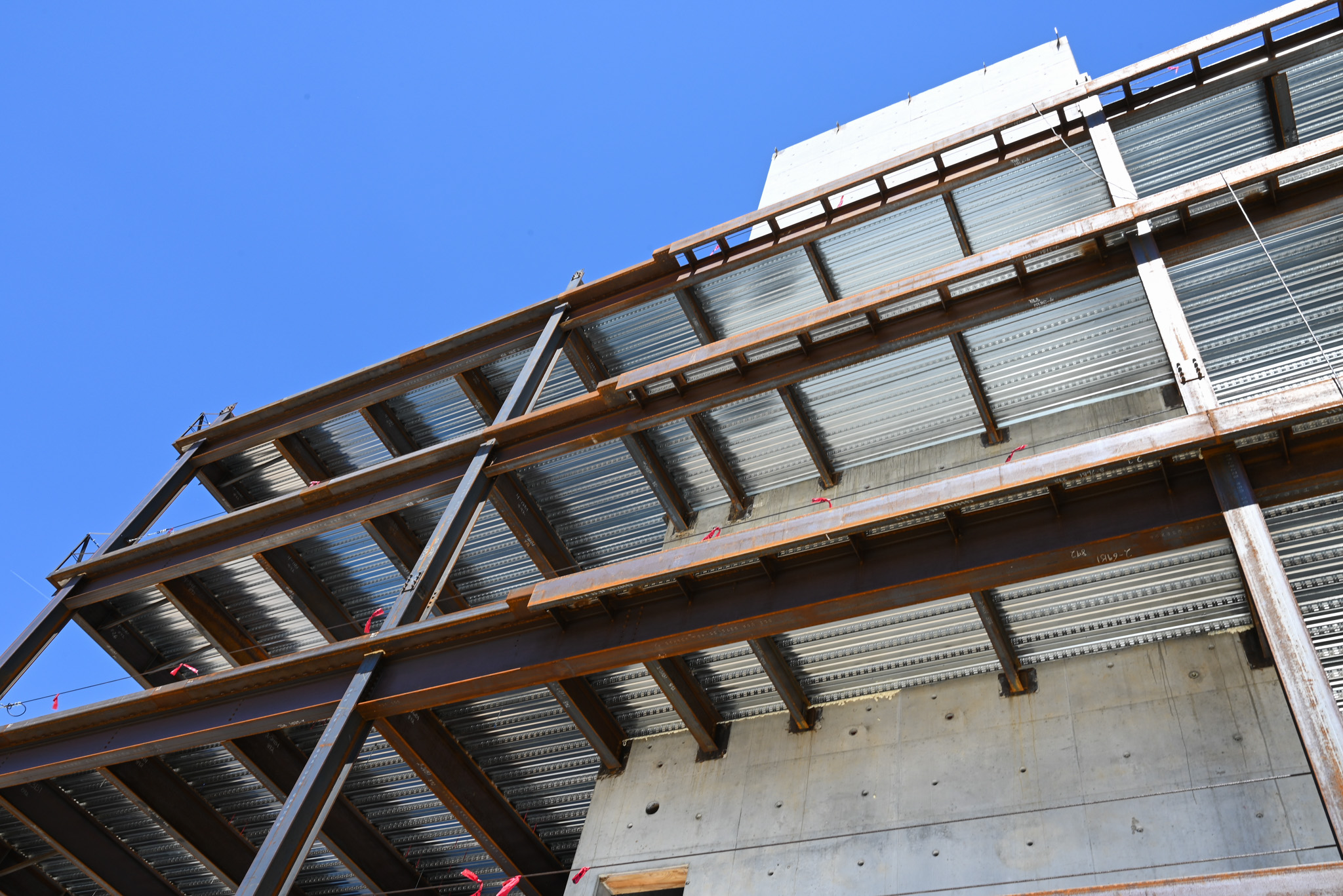 A low-angle view of a steel and concrete building under construction against a clear blue sky.