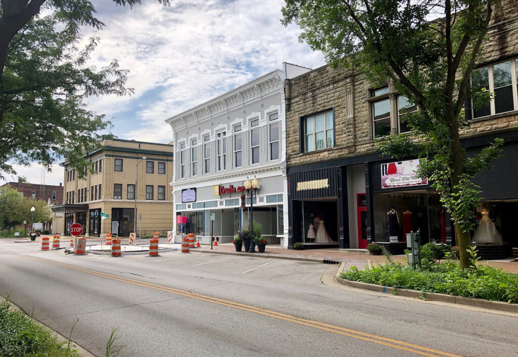 A quiet downtown street with bridal shops, orange traffic barrels, trees, and historic buildings under a partly cloudy sky.