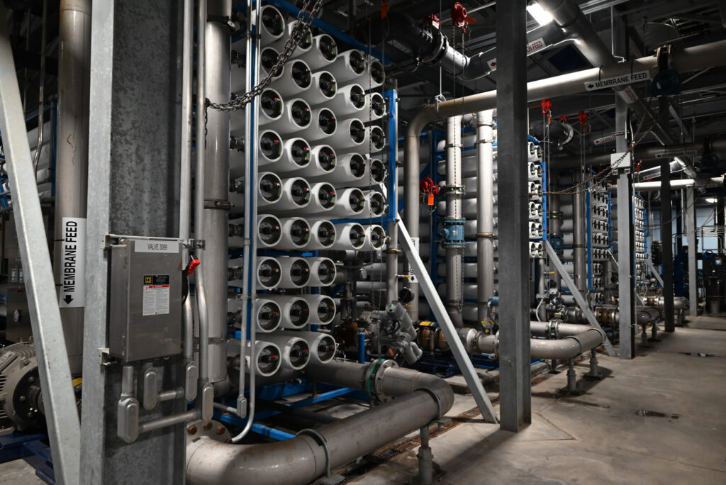 Rows of cylindrical filters and pipes inside an industrial water treatment facility, with labeled controls and metal supports visible throughout the equipment.