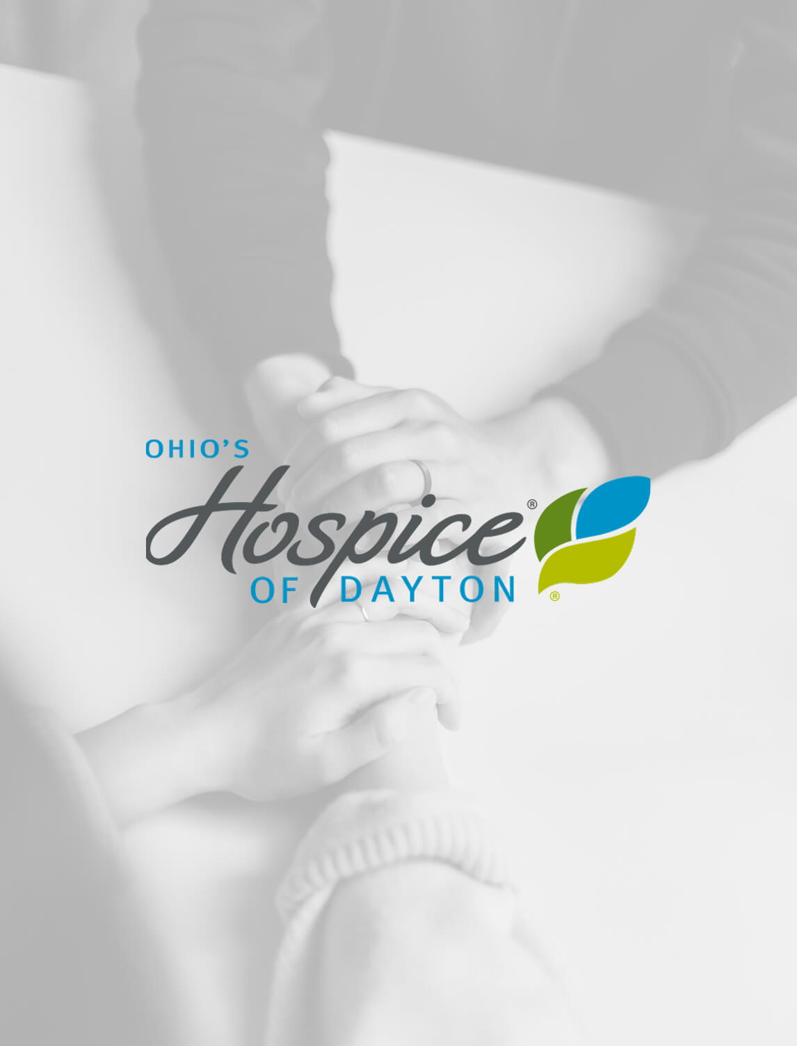 Two people hold hands across a white table. The logo for Ohios Hospice of Dayton appears centered over the image, featuring stylized text and blue and green leaf graphics.