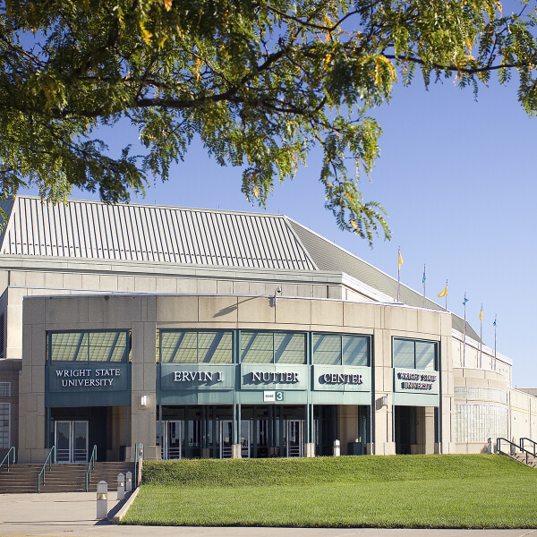Front view of the Ervin J. Nutter Center at Wright State University, with a tree branch above, glass entrance doors, and signs for the Nutter Center and WSU School of Business visible.
