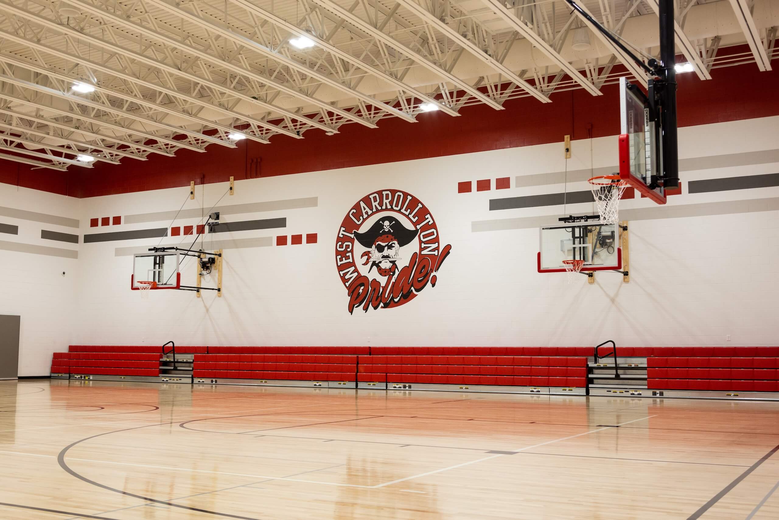 High school gym with red bleachers, two basketball hoops, and West Carrollton Pride! painted on the wall with a pirate mascot in the center.